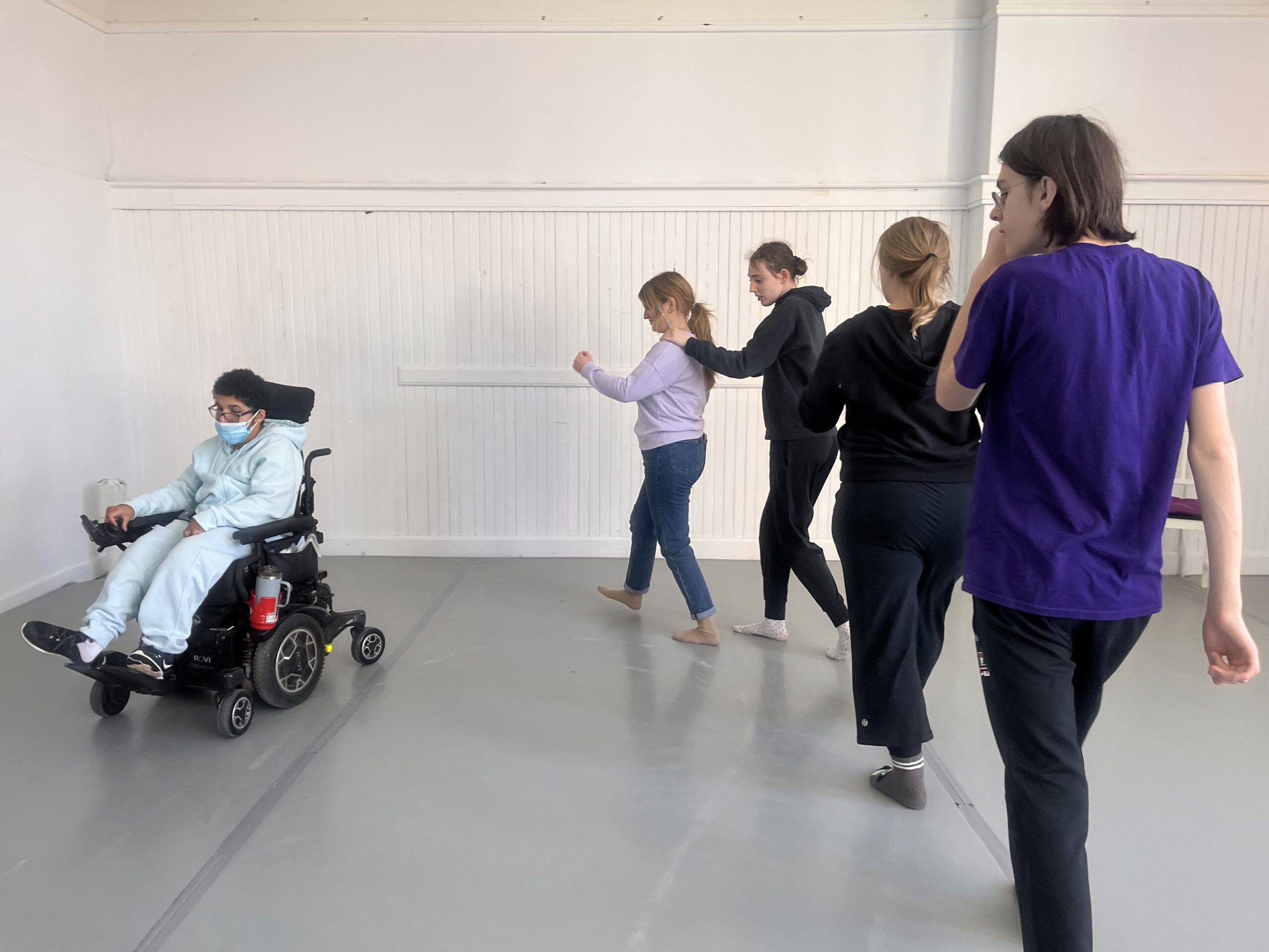 a group of people in a room with one person in a wheelchair leading a line