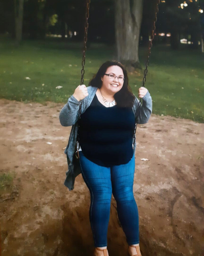 A photo of Adreena Benner, smiling as she sits on a swing in a park